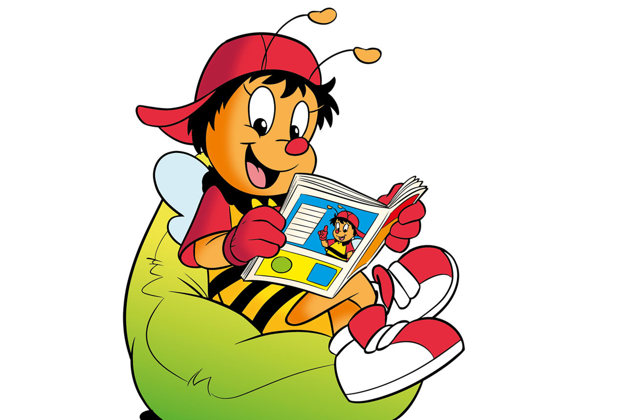 Sumsi sitzt in einem grünen Sitzkissen und liest ein Heft