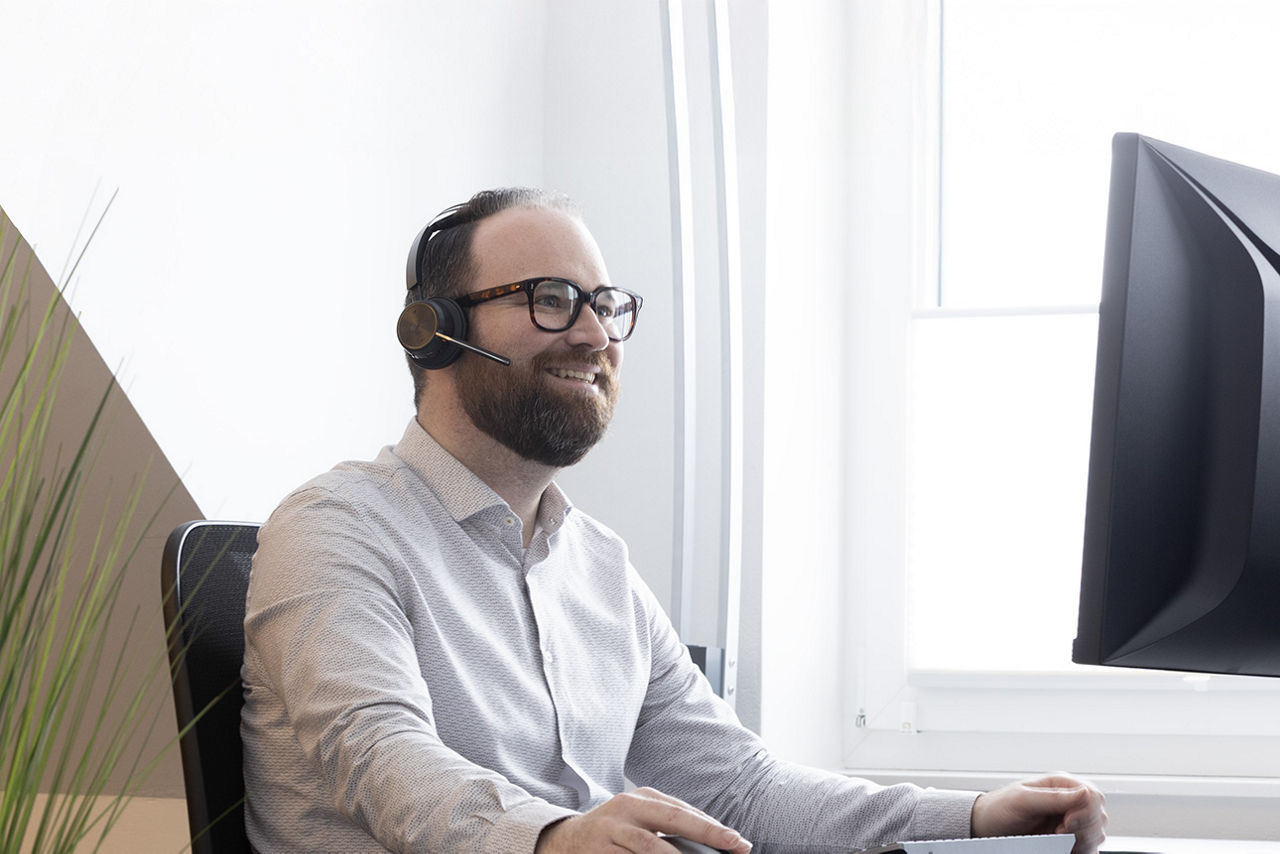 Ein Kollege sitzt mit einem Headset vor seinem Computer