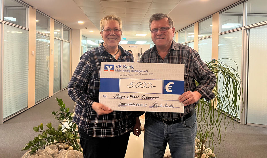 Das Bild zeigt die Gewinner des Gewinnsparens, die stolz einen Scheck über 5.000 Euro halten. Sie lächeln glücklich in einer festlichen Atmosphäre.