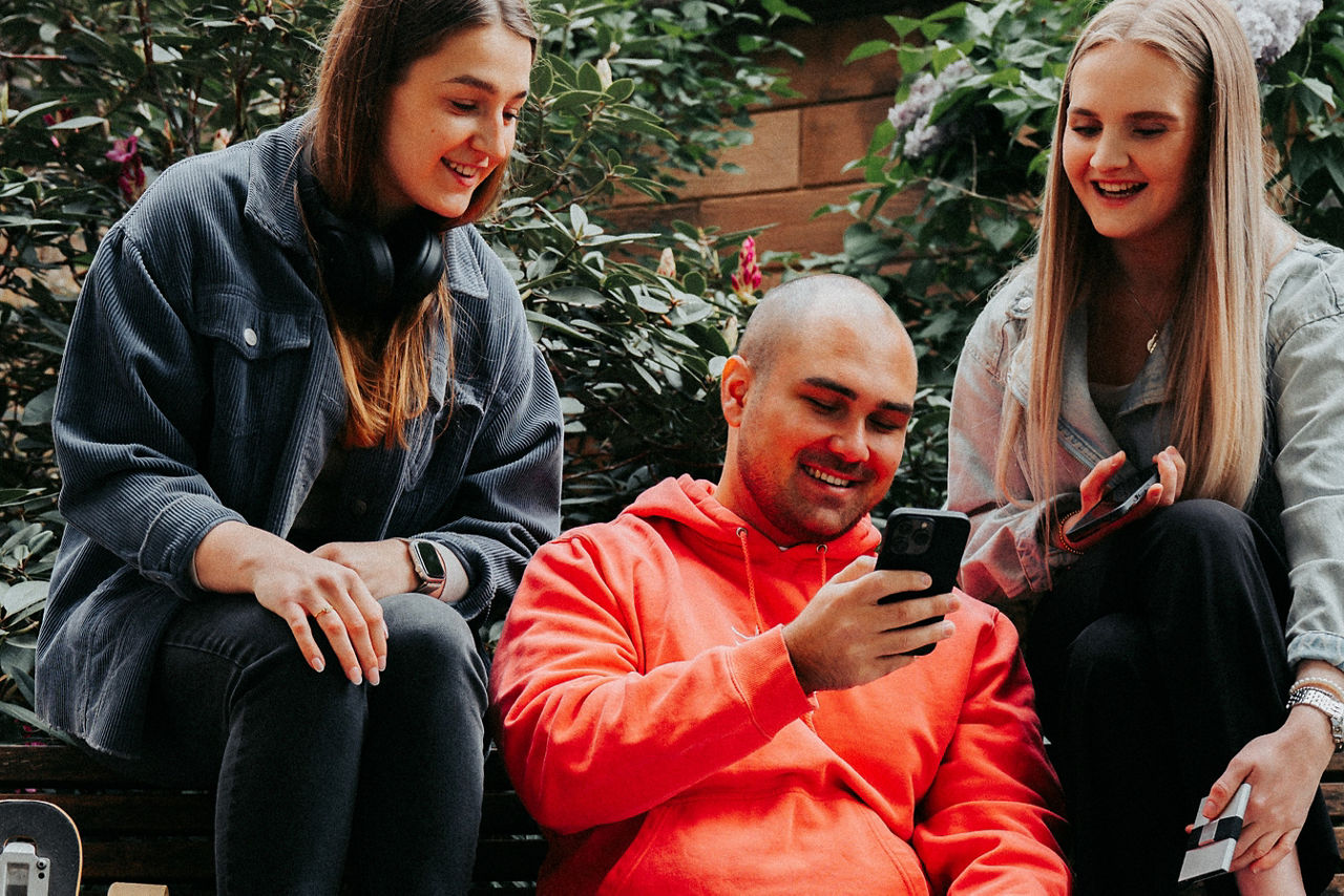 Drei Personen sitzen draußen auf einer Bank und schauen jeweils auf ihr Smartphone.