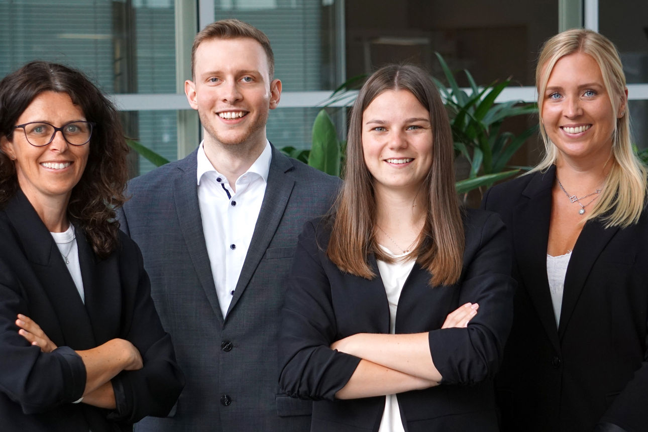 Drei Frauen und ein Mann in Sakkos lächeln in die Kamera