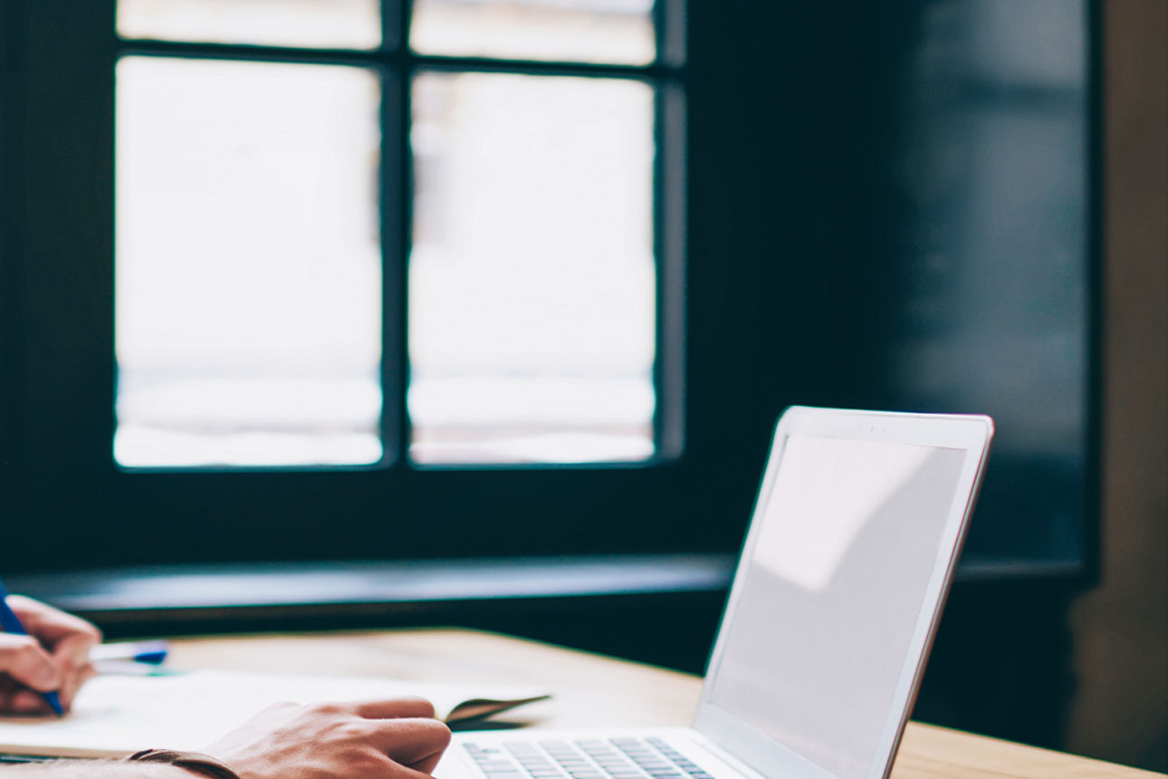 Ein Mann schreibt etwas auf einen Block und hat vor sich einen Laptop stehen.