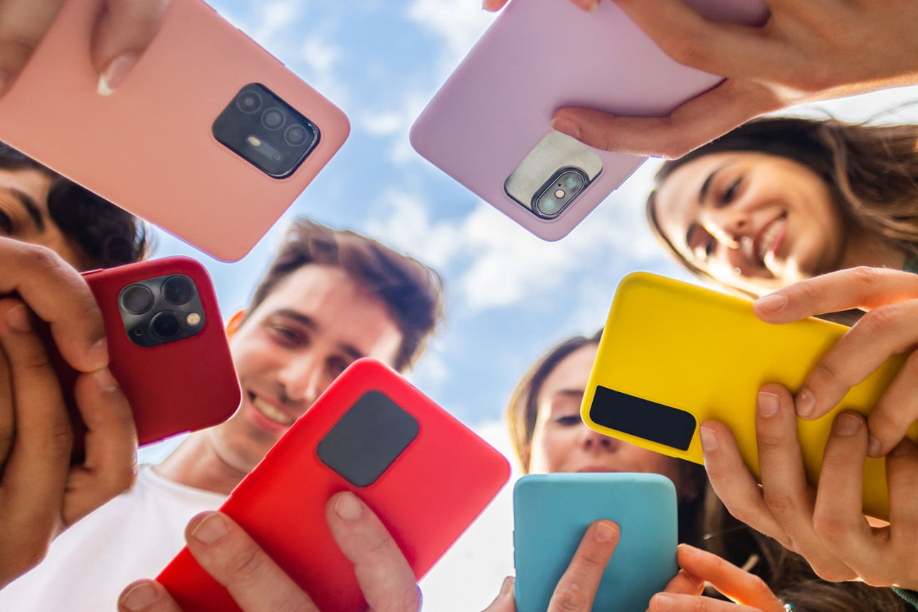 Eine Gruppe mit Menschen, die sich in einem Kreis versammelt haben und alle auf ihr Handy schauen.