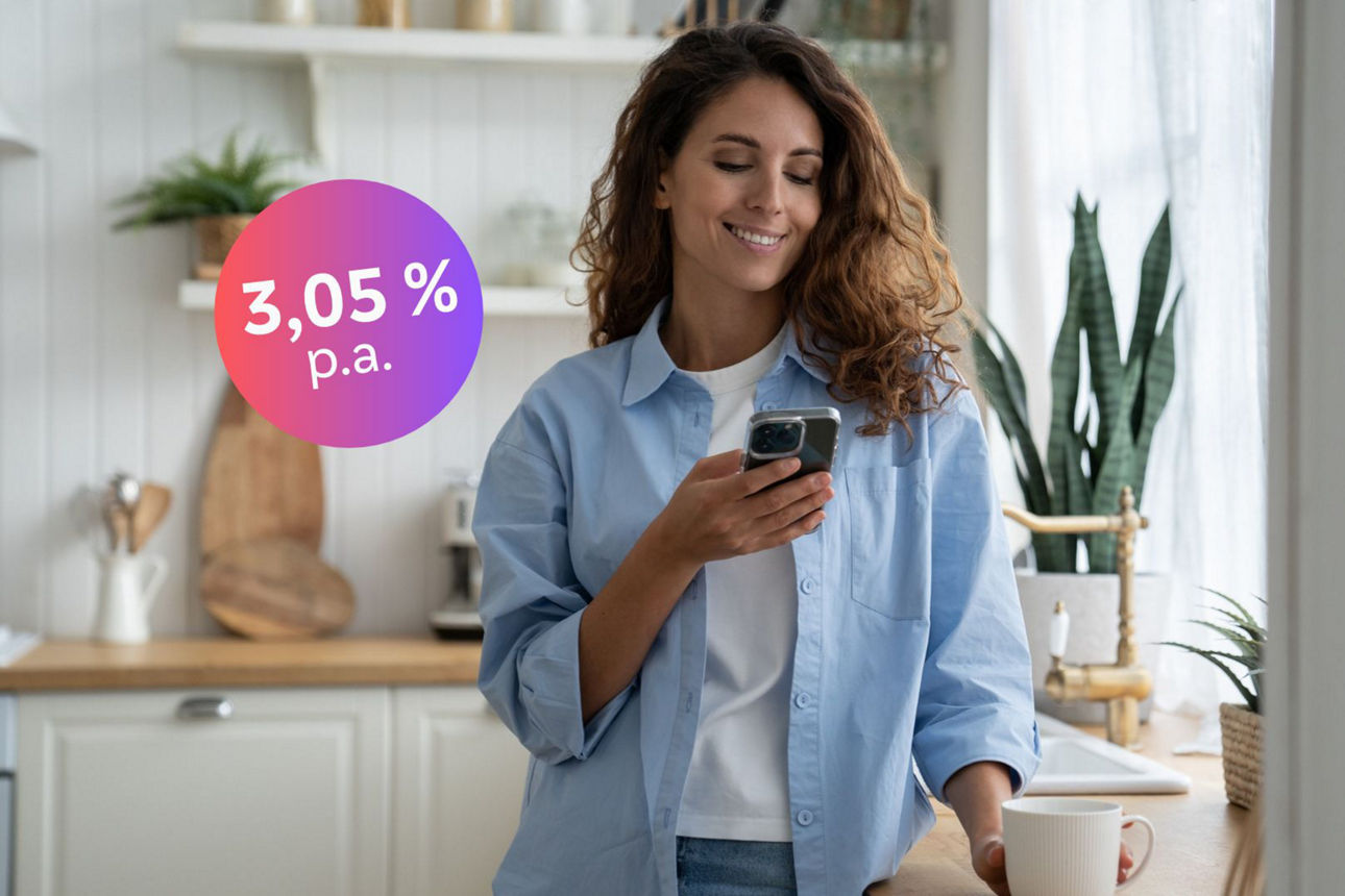 Frau steht mit Handy in der Hand in der Küche und lächelt, Störer mit 3,05% ist zu sehen