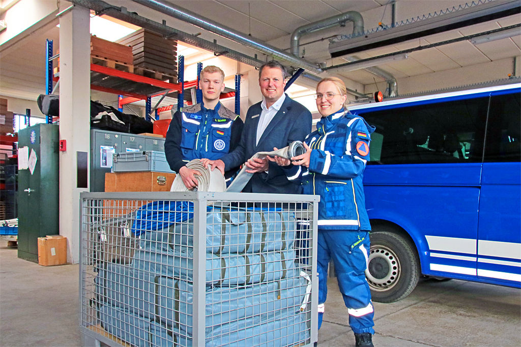 Zwei THW Mitglieder mit einem Bankmitarbeiter vor einer Gitterbox
