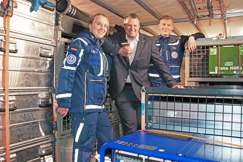 Zwei THW Mitglieder mit einem Bankmitarbeiter vor einer Gitterbox