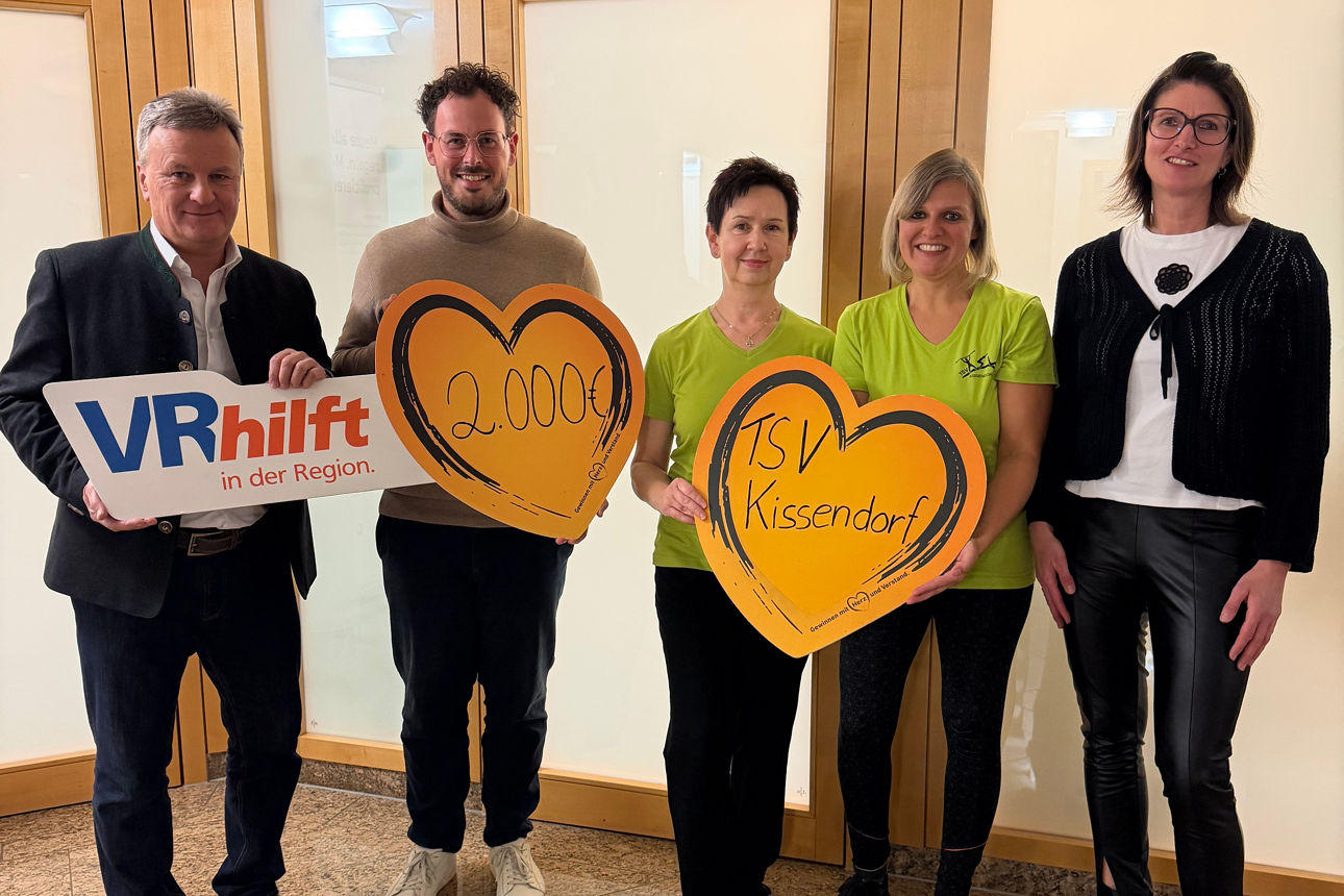 Fünf Personen mit Herzschildern und „VR hilft“-Logo, gemeinsame Spendenübergabe in Innenraum