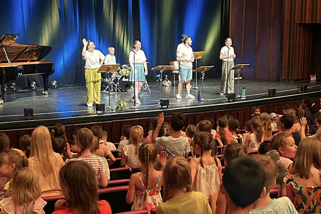 Auf der Bühne stehen SängerInnen, die mit Kindern singen