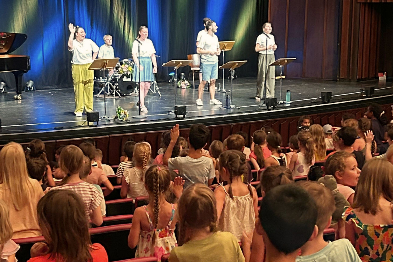 Auf der Bühne stehen SängerInnen und im Publikum sitzen Kinder, die mitsingen