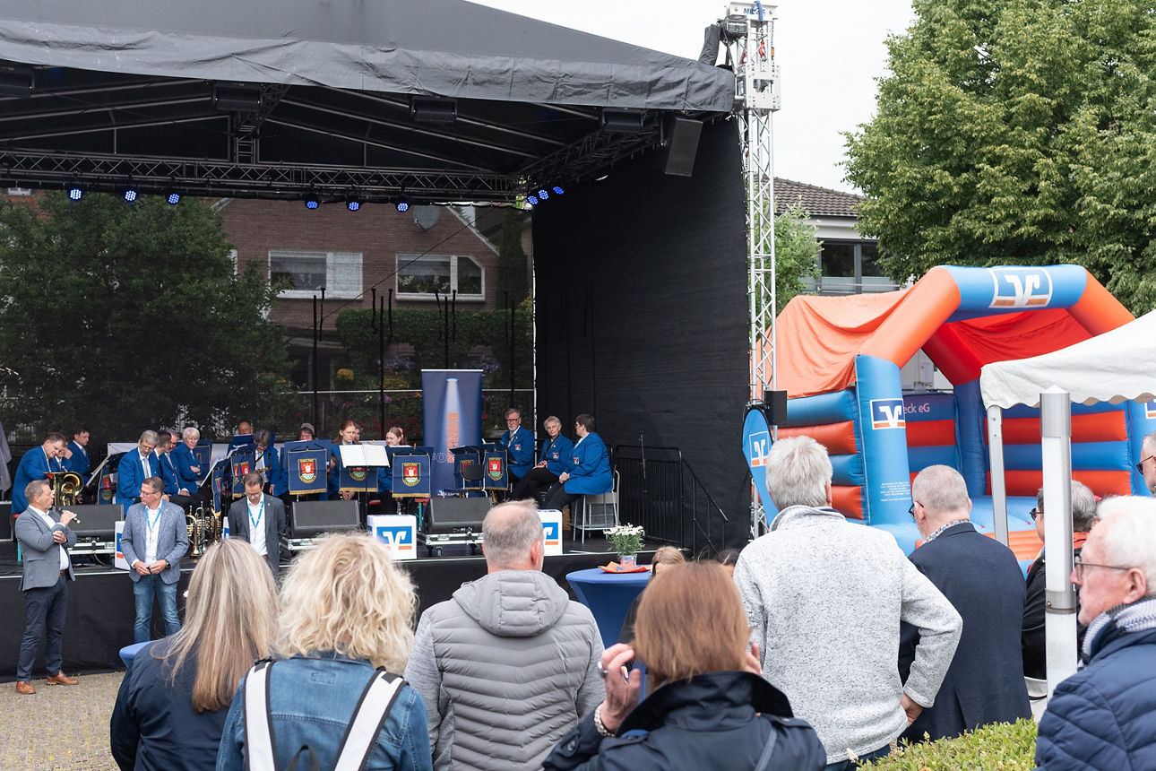Personen stehen vor einer Bühne, auf der Kapelle Einklang Schermbeck musiziert.