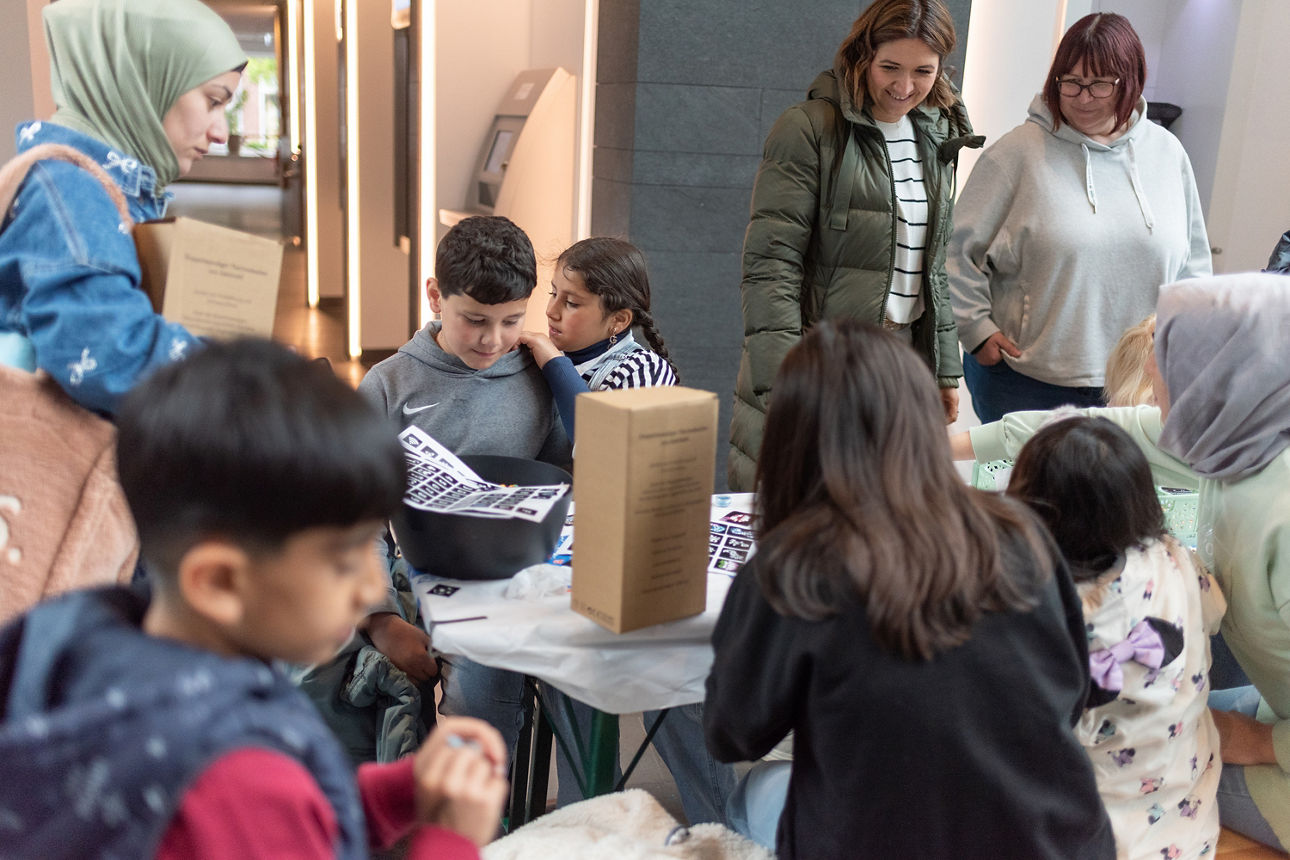 Viele Kinder und Erwachsene an einem Basteltisch