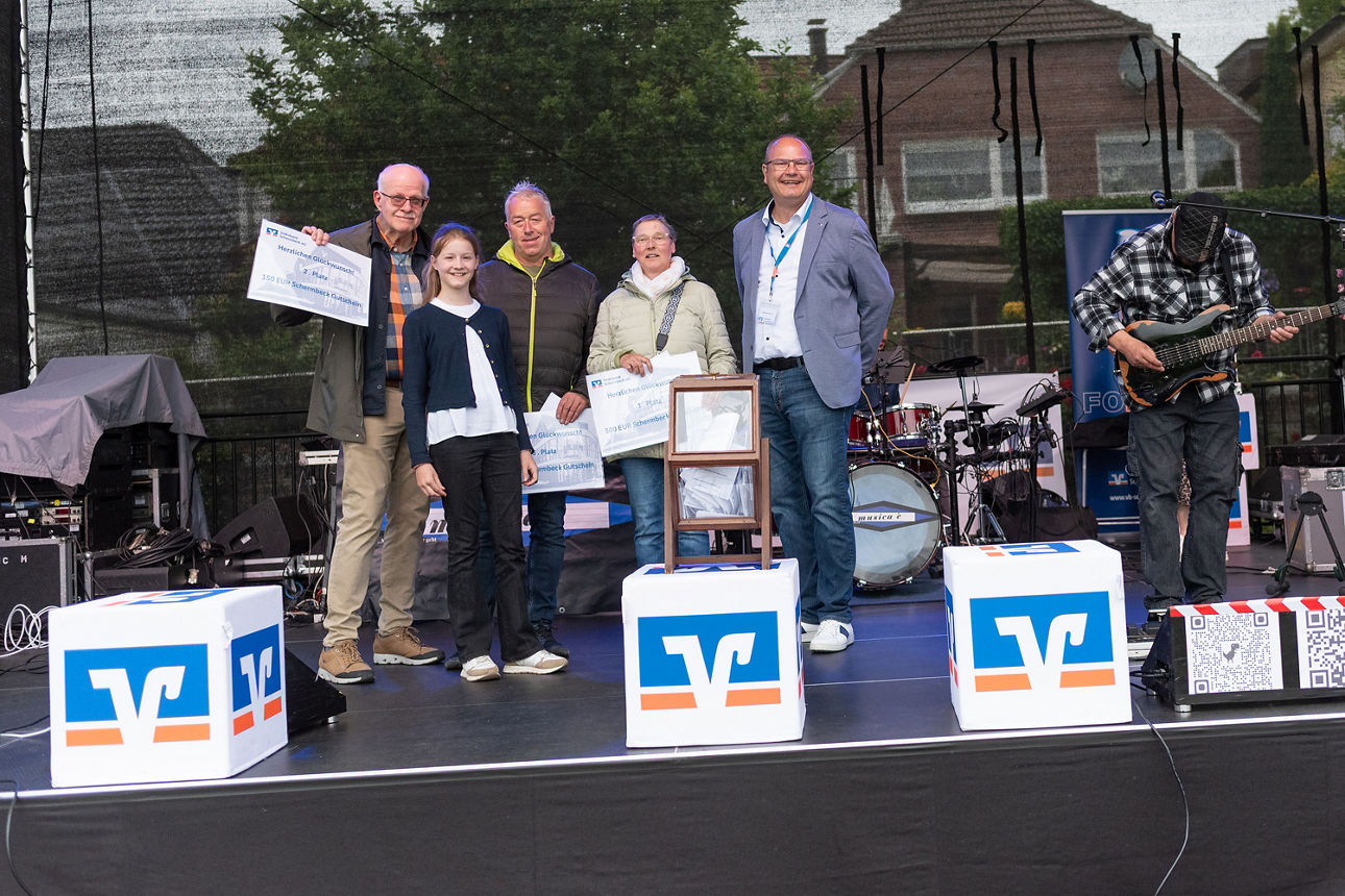 Vier Personen mit Gewinn-Urkunden und ein Mitarbeiter der Volksbank Schermbeck auf einer Bühne