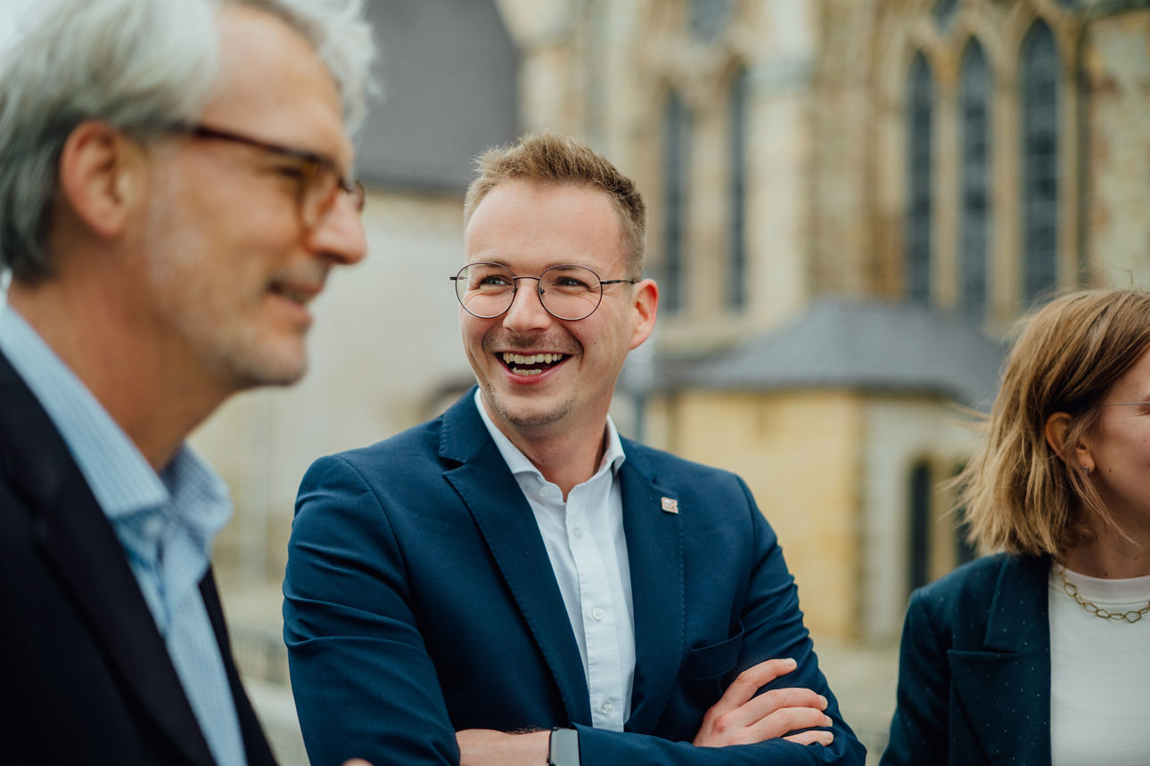 Drei Mitarbeitende stehen vor einer Kirche und lachen