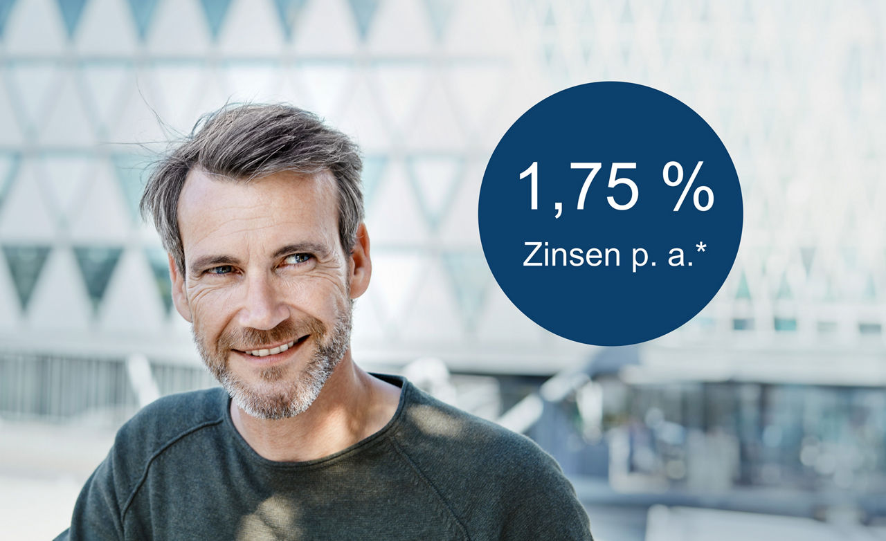 Mann mit Bart und grauem Pullover steht vor Glasfassade daneben Störer mit Text 1,75% Zinsen p. a.*