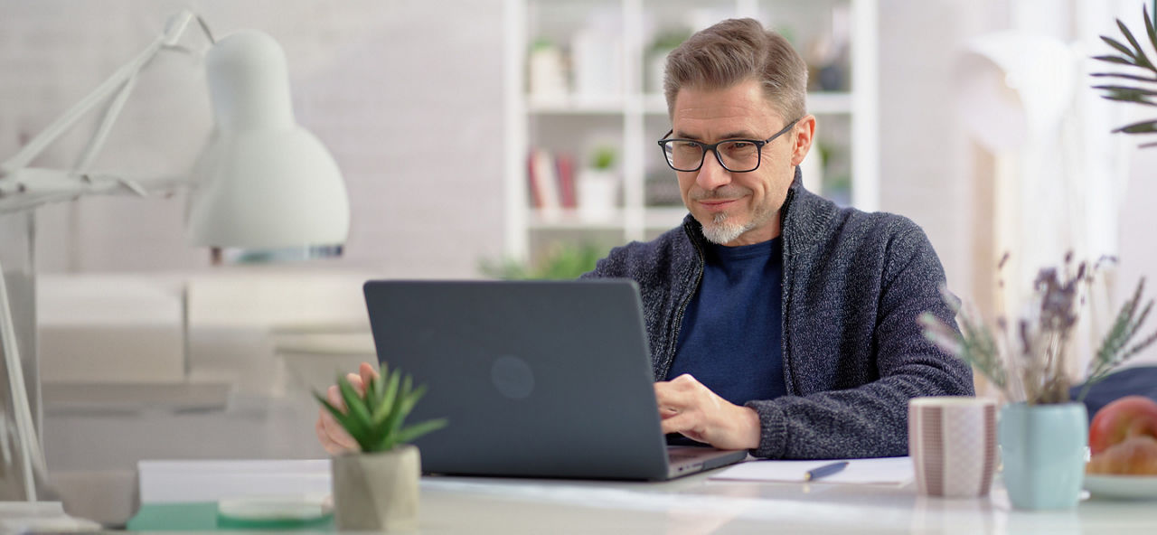 Mann mittleren Alters mit Brille sitzt an einem Laptop.