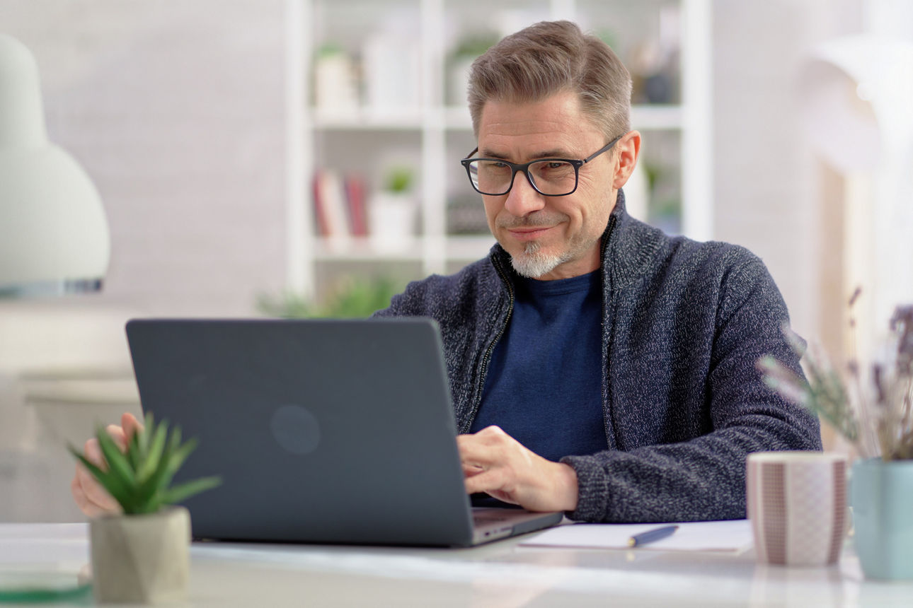 Mann mittleren Alters mit Brille sitzt an einem Laptop.