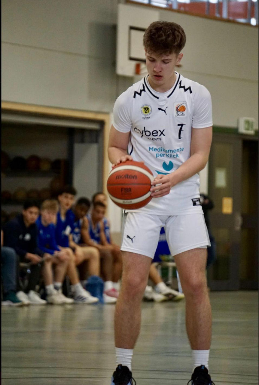 Junger Basketballspieler steht in einer Sporthalle an der Freiwurflinie und bereitet einen Wurf vor.