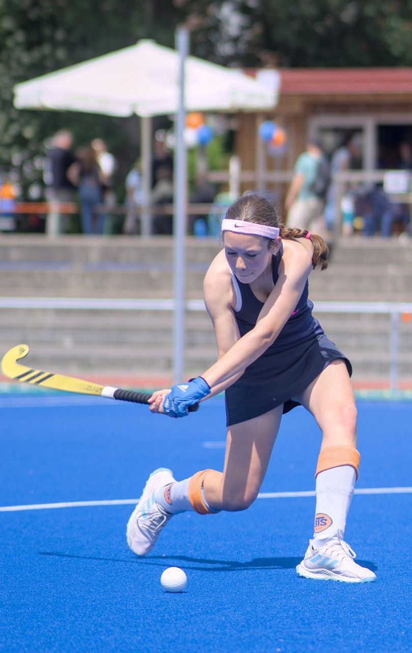 Hockeyspieler auf blauem Kunstrasen führt den Ball mit dem Schläger während eines Spiels oder Trainings auf einem Hockeyplatz