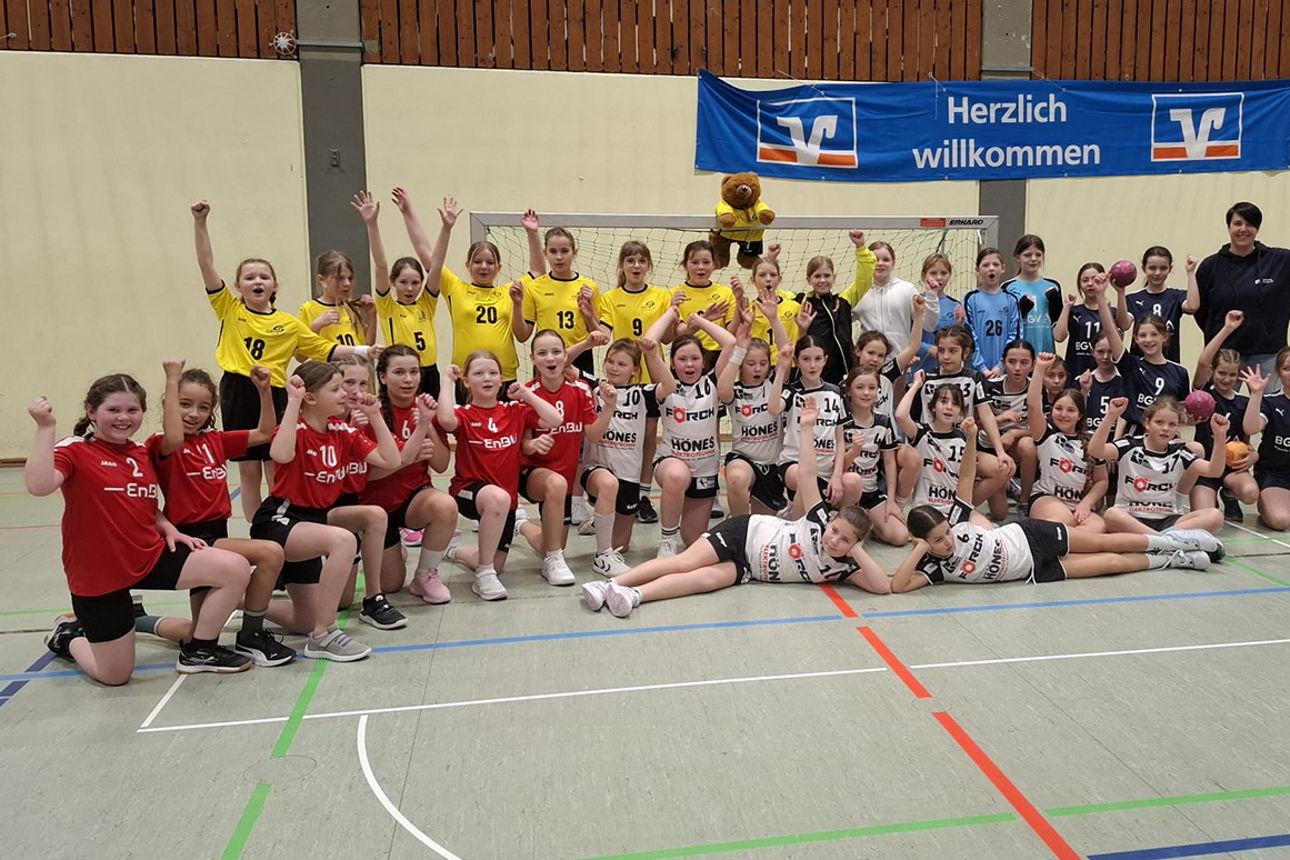 Eine große Gruppe junger Handballerinnen jubelt für ein Gruppenfoto in einer Sporthalle