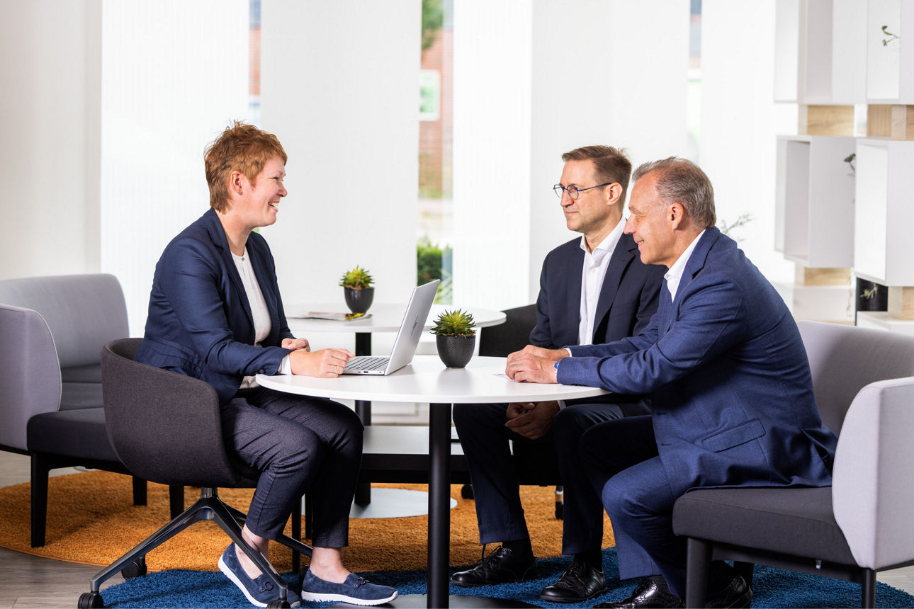 Eine Mitarbeiterin und zwei Mitarbeiter des Private Bankings unterhalten sich an einem Tisch