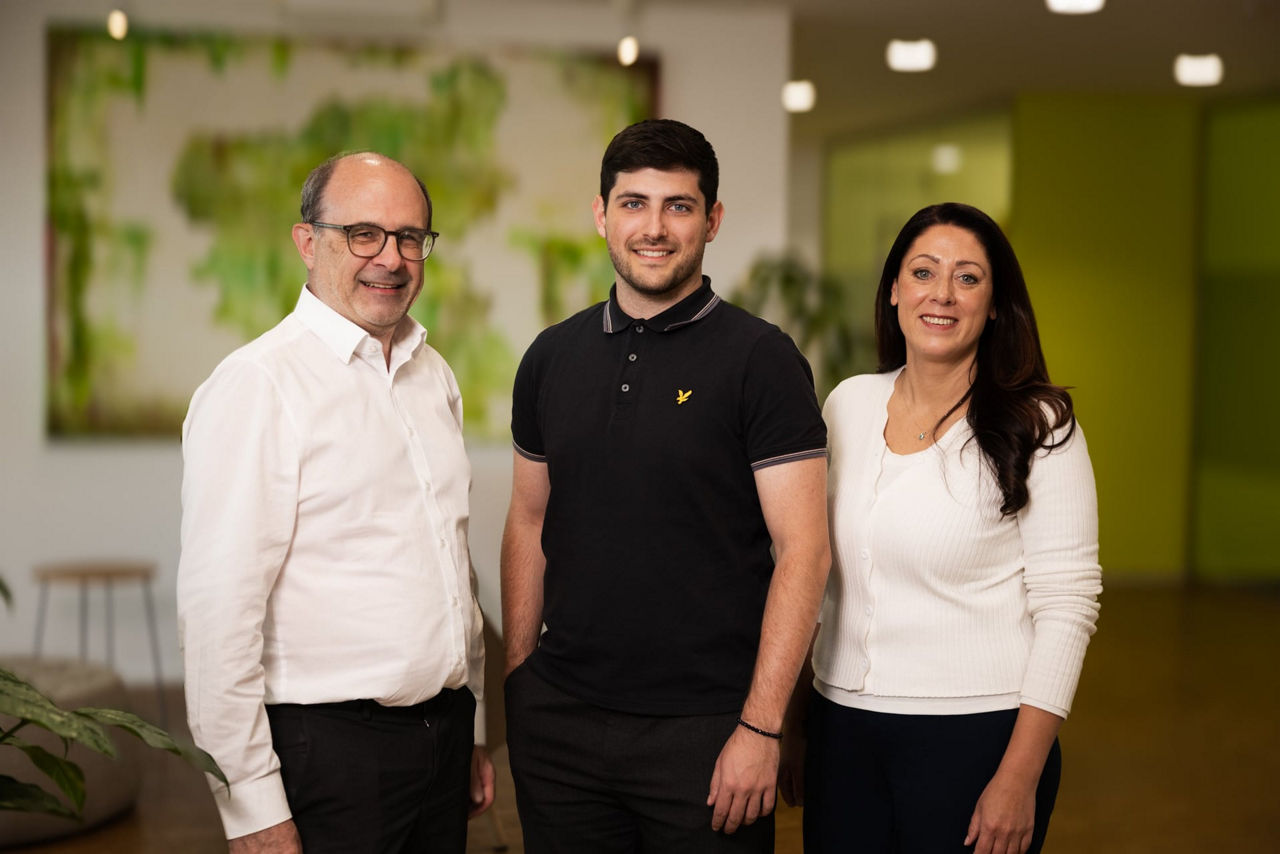 Zwei Männer und eine Frau schauen lächelnd in die Kamera