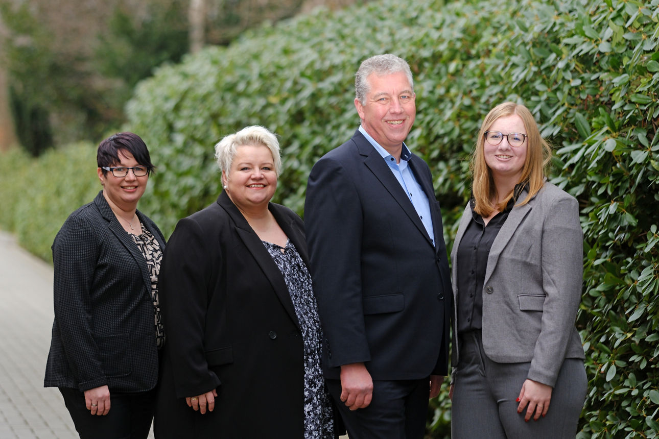 Vier Mitarbeiterinnen und Mitarbeiter der Raiffeisenbank vor einer Hecke