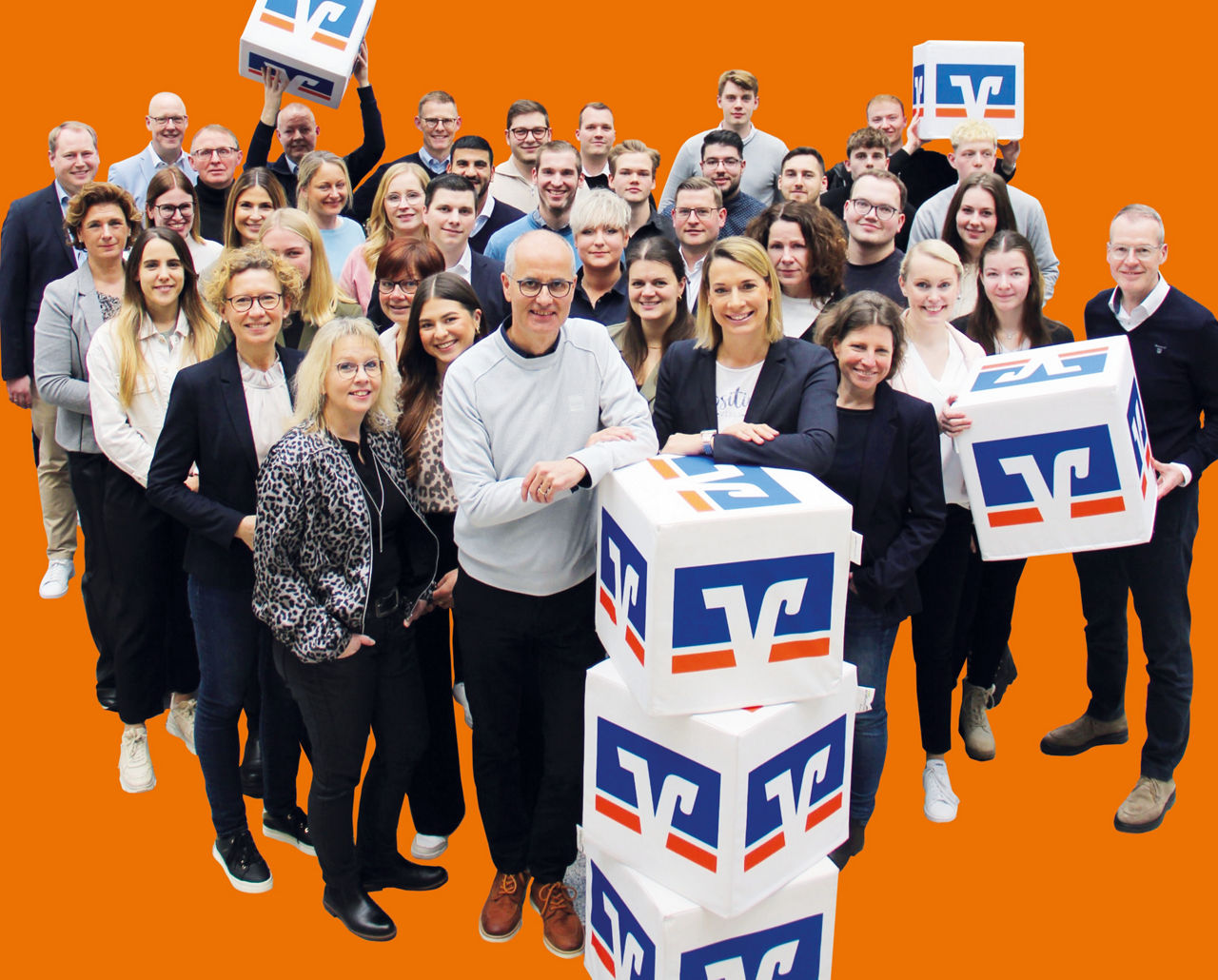Team der Volksbank Baumberge eG mit Volksbank Würfeln vor orangem Hintergrund