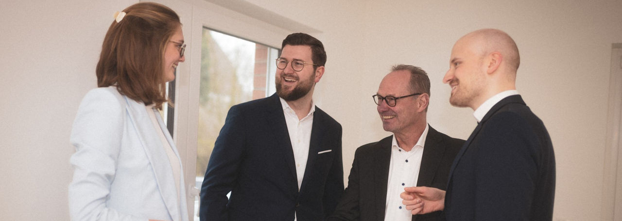 Vier Personen in Businesskleidung unterhalten sich lächelnd in einem hellen Besprechungsraum.