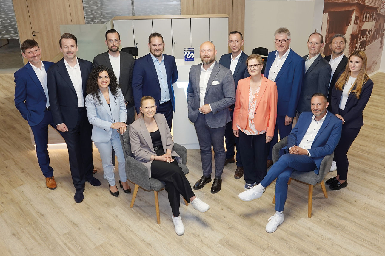Eine bunte Gruppe von Berufstätigen – Männer und Frauen – posiert in einer Büroumgebung für ein Gruppenfoto.