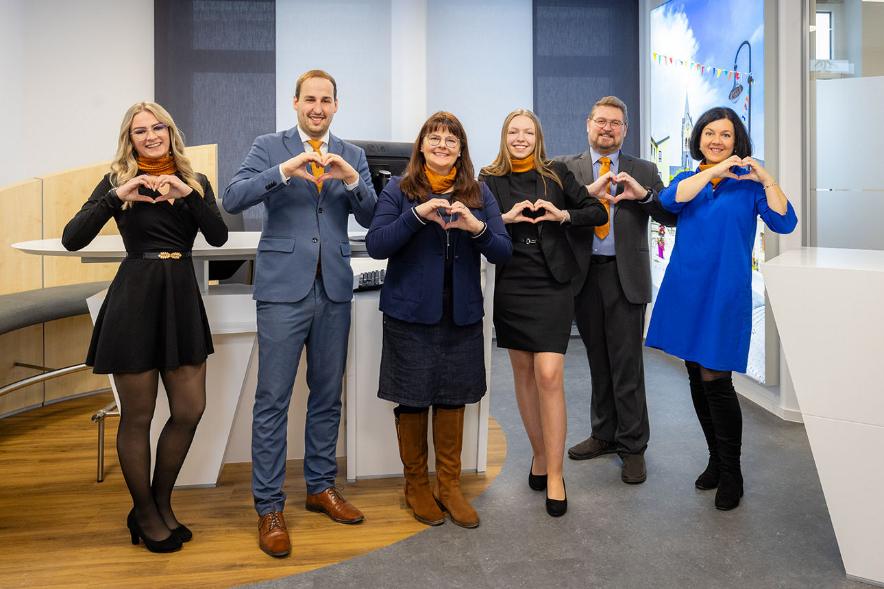 Mitarbeiter der VR Bank Bayreuth-Hof eG stehen in einer Filiale und formen mit den Händen Herzen