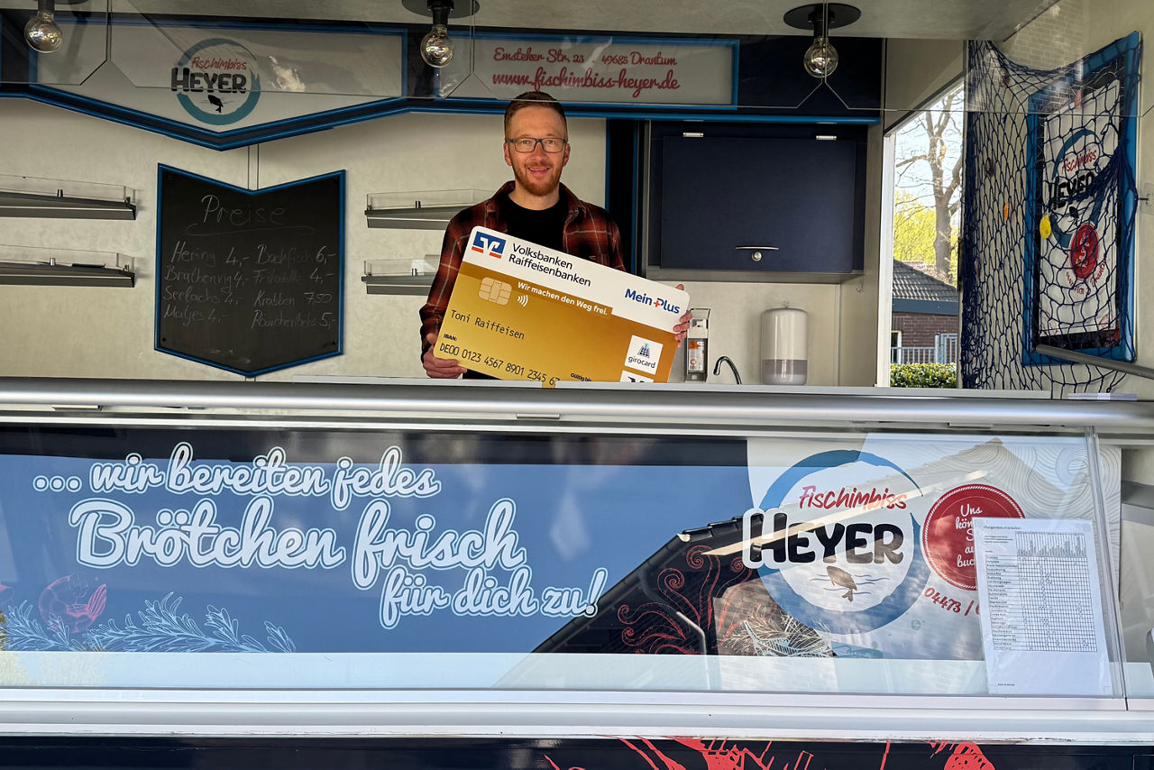 Mann hinter Fischtheke mit einer Bankkarte in der Hand