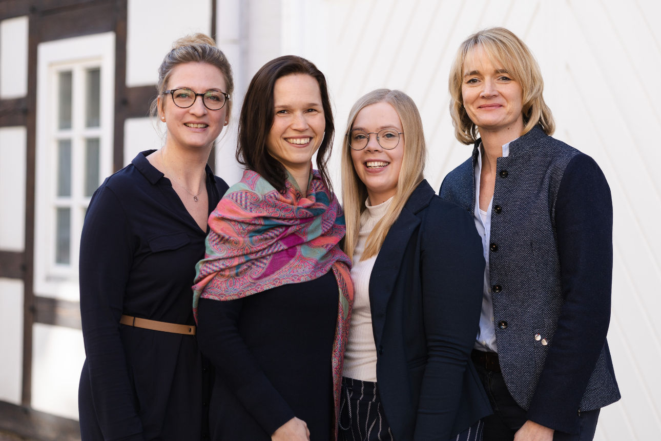 Vier Personen, die dicht beieinander stehen und im Freien vor einem Gebäude posieren.