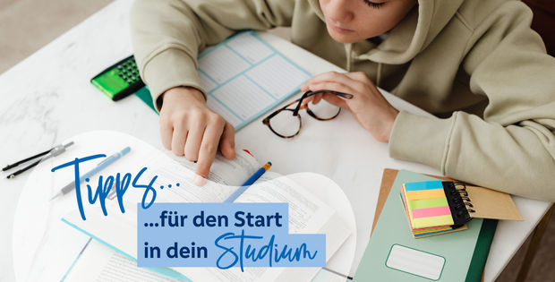 Person die an einem Schreibtisch sitzt und mit dem Finger in einem Buch liest 