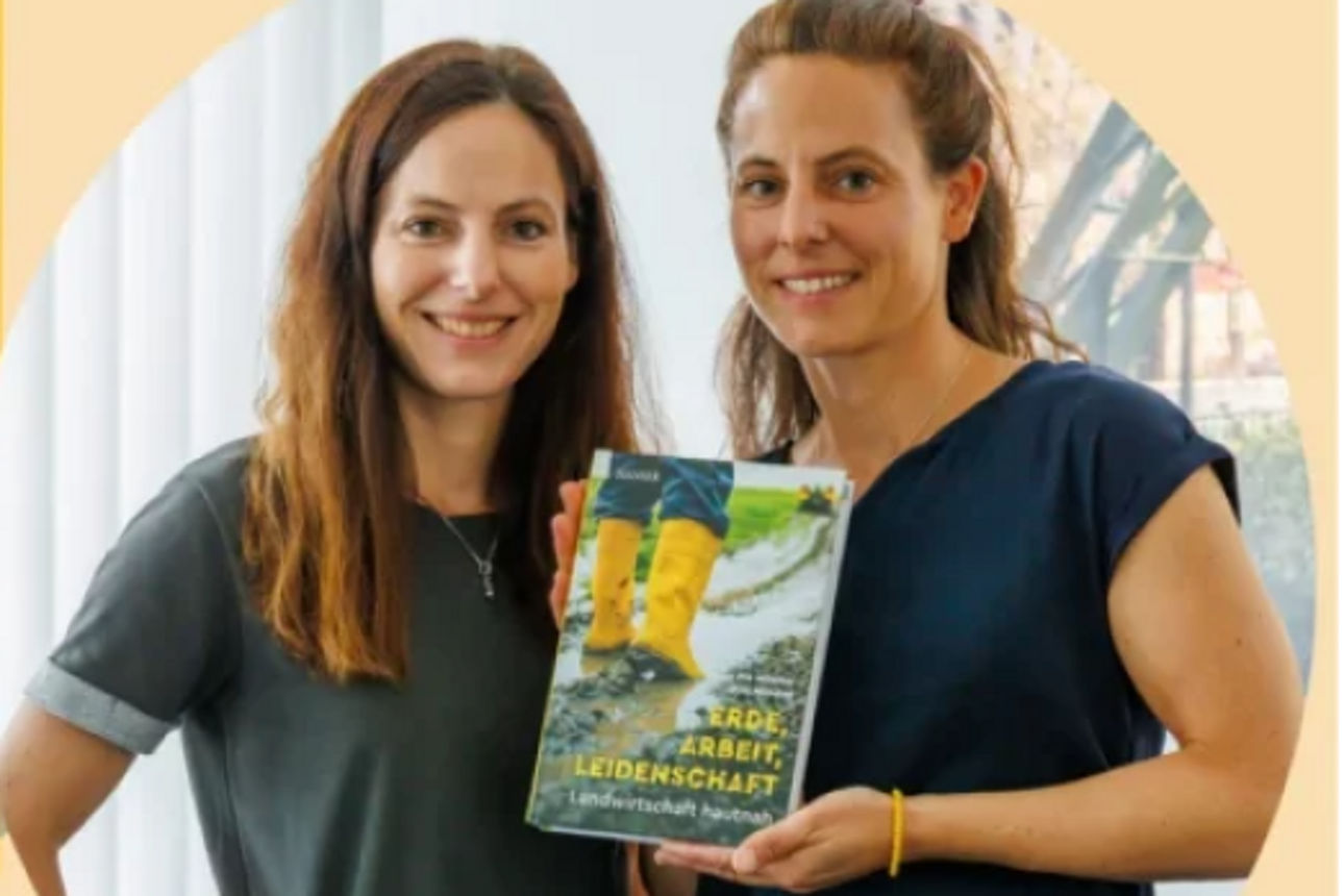 Zwei Frauen lächeln in die Kamera und halten ein Buch