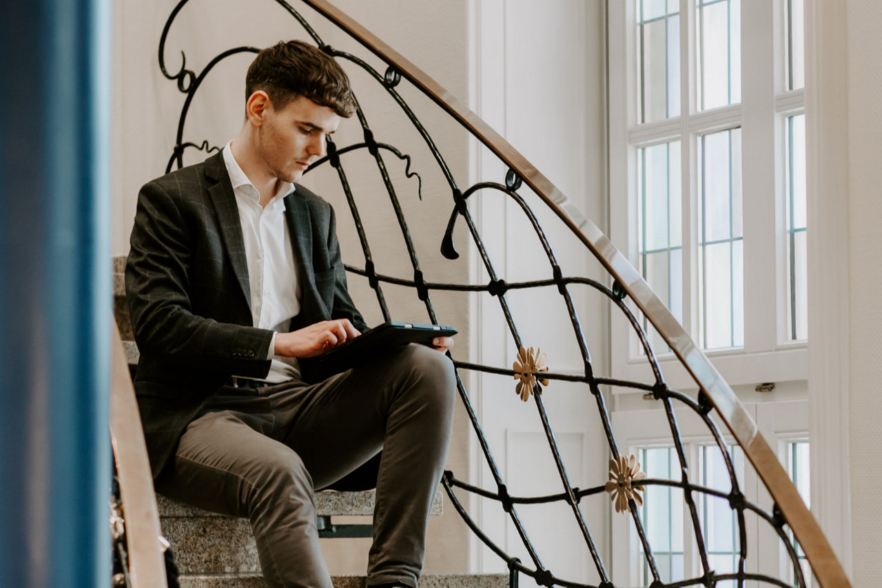 Ein Mann sitzt auf einer Treppe und schaut auf ein Tablet