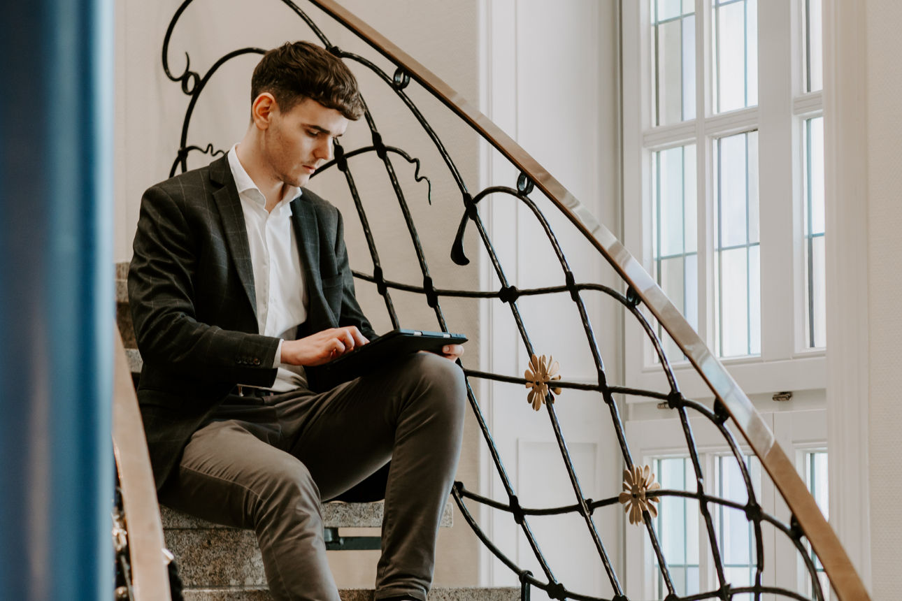 Ein Mann sitzt auf einer Treppe und schaut auf ein Tablet
