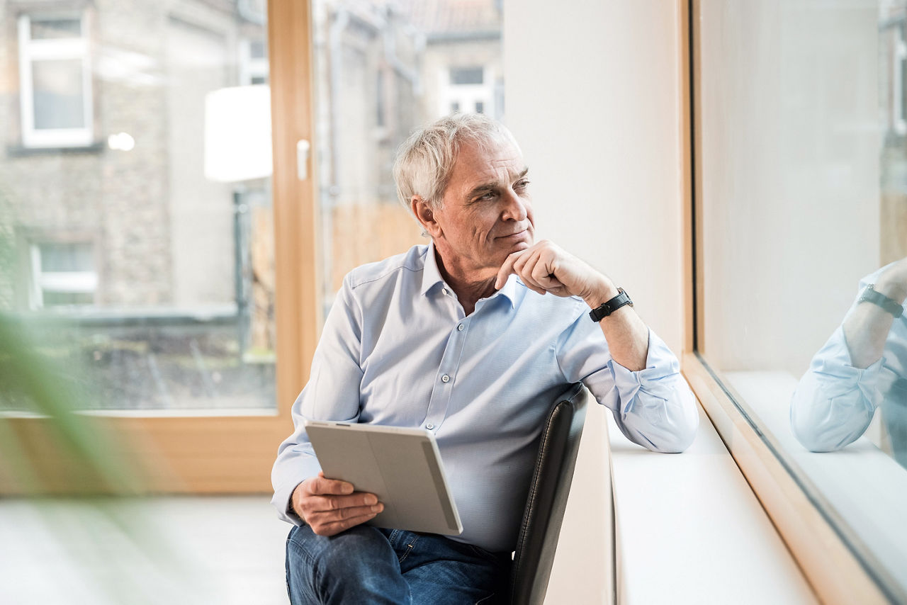 Älterer Herr sitzt mit Laptop am Fenster