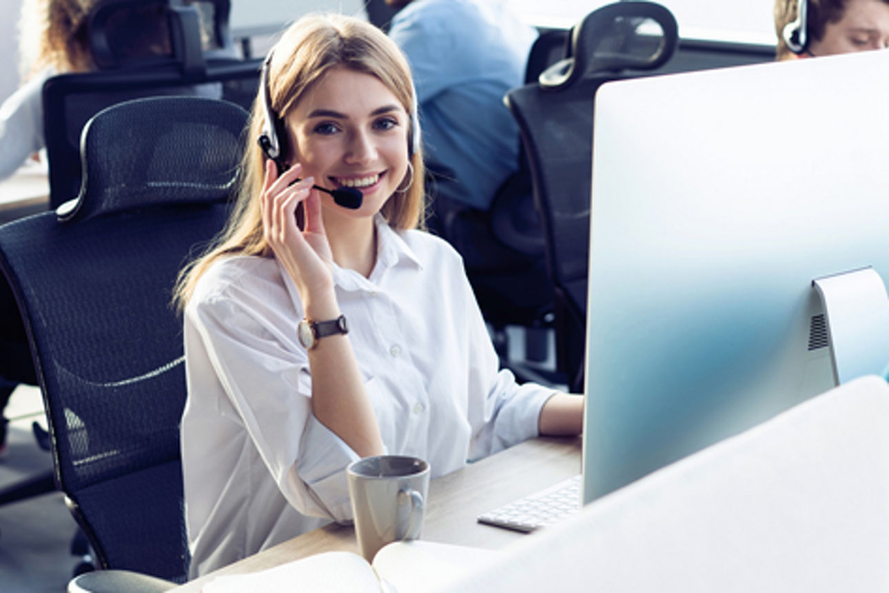 Frau mit Headset am Schreibtisch vor einem PC