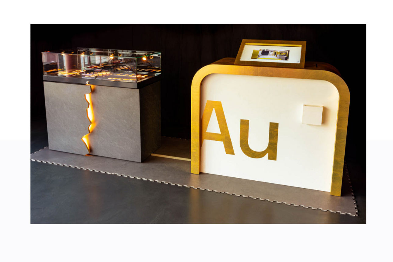 Zwei Ausstellungselemente mit dem chemischen Symbol für Gold „Au“ auf einer beleuchteten Präsentationsfläche in einem dunklen
