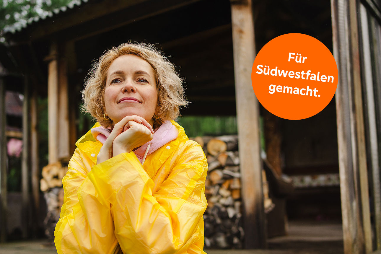 Eine Frau in einer gelben Regenjacke steht auf ihrer Terrasse
