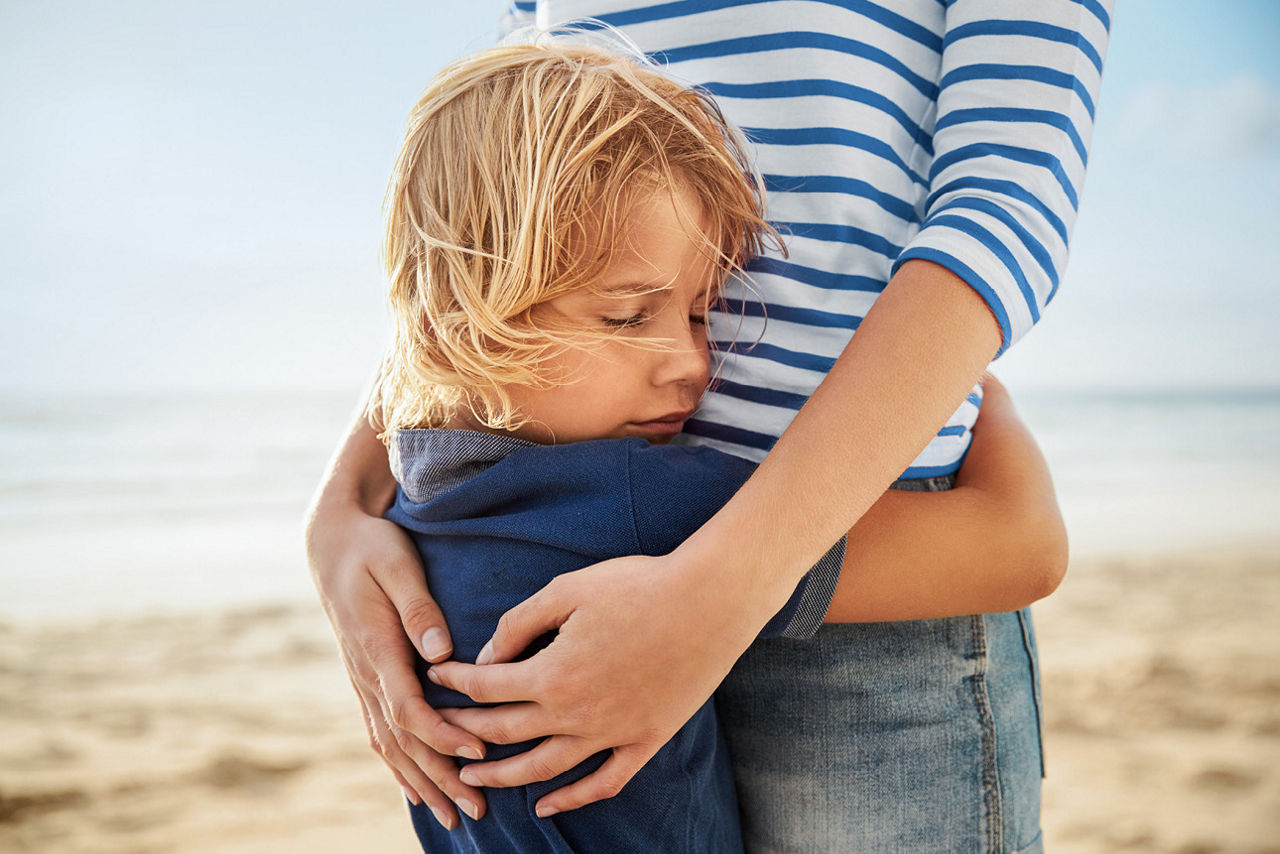 Kind steht am Strand und umarmt die Mama