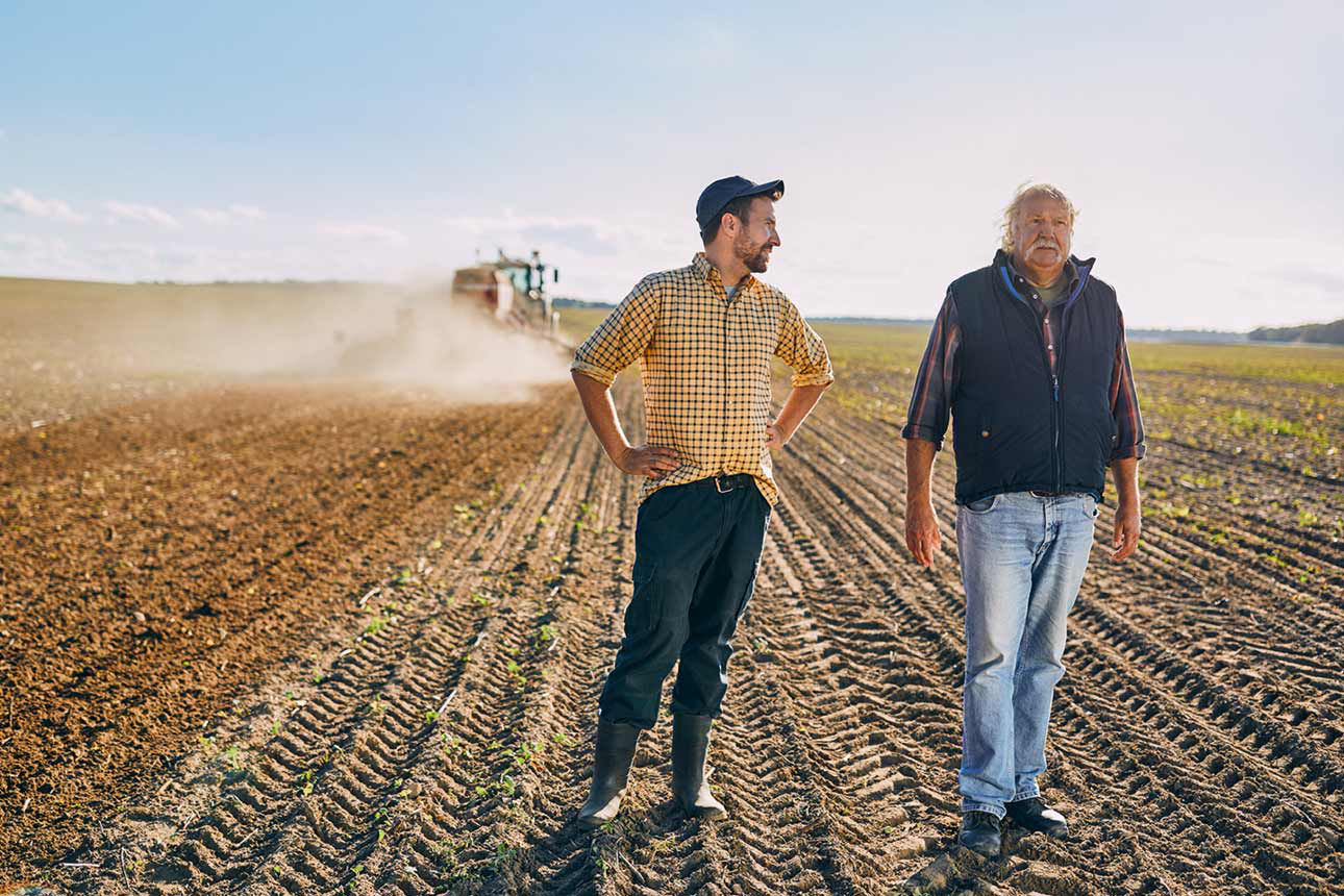 Zwei Männer auf einem frisch gepflügten Feld, im Hintergrund ein Traktor.