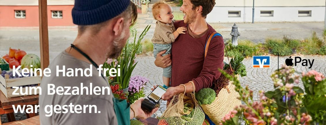 Mann mit Kind auf dem Arm will mit Handy im Blumenladen bezahlen