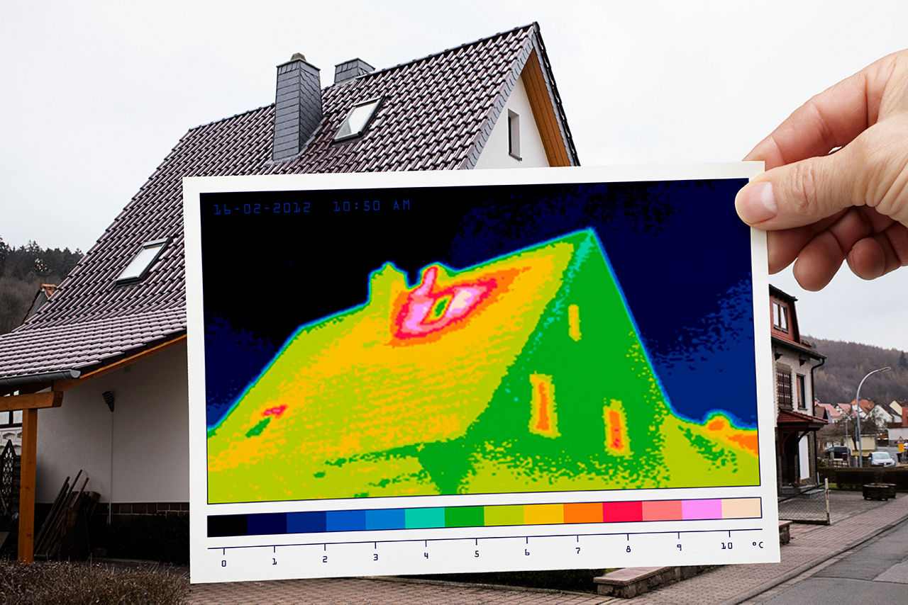 Hand hält Auszug eines Energieausweises vor ein Haus 