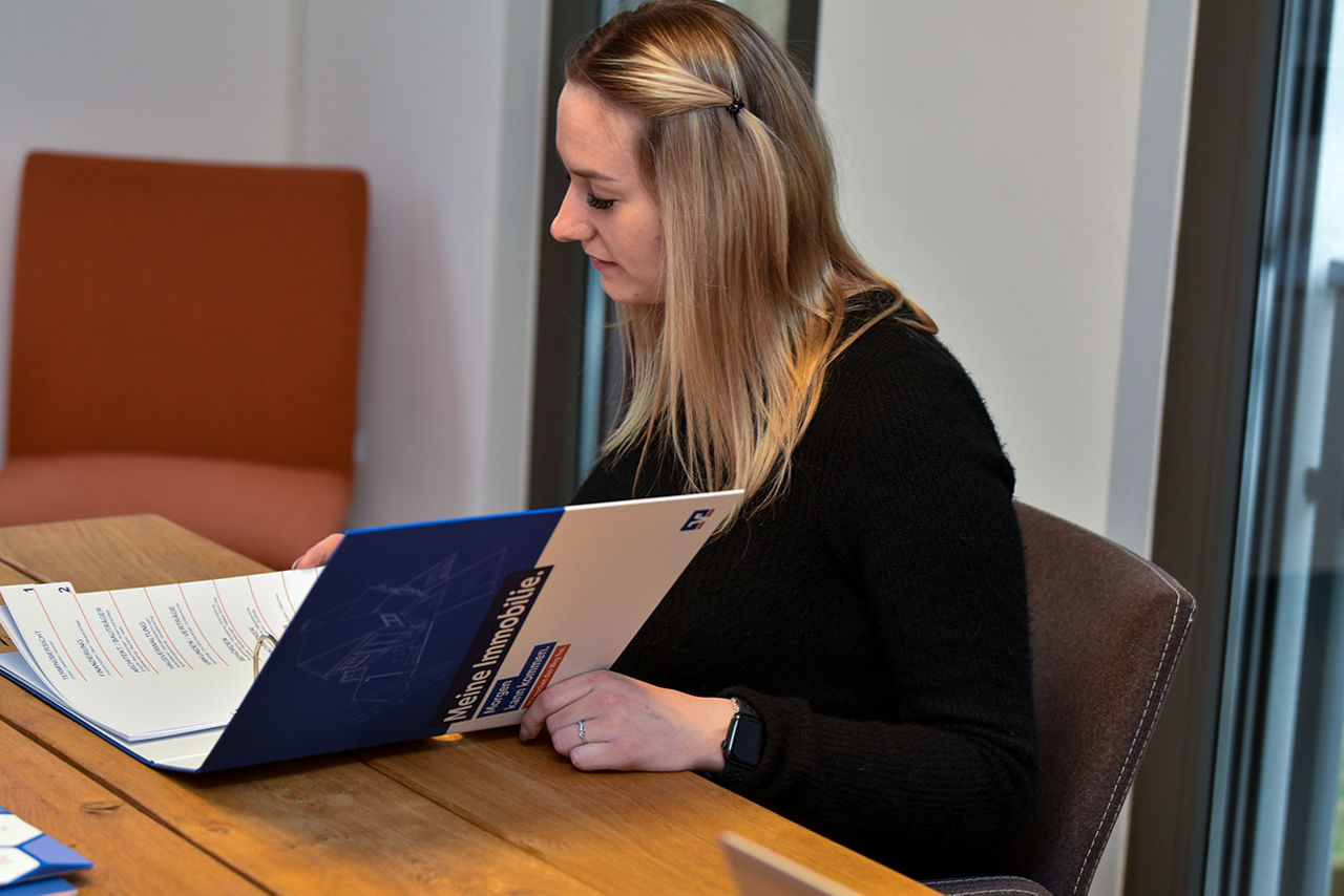 Junge blonde Frau sieht an einem Tisch und blättert durch einen Ordner