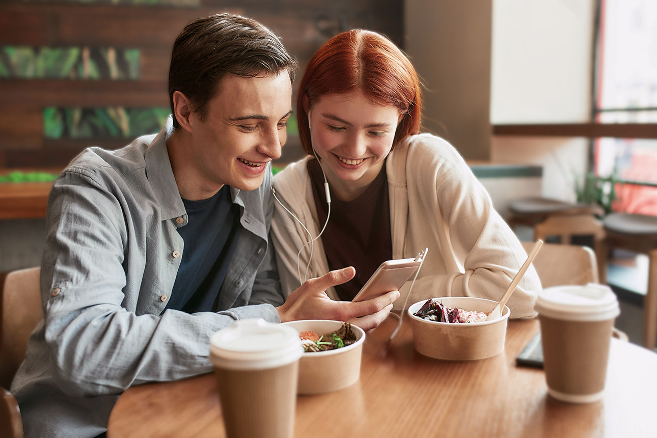 Zwei Jugendliche sitzen in einem Café und schauen auf ein Smartphone.