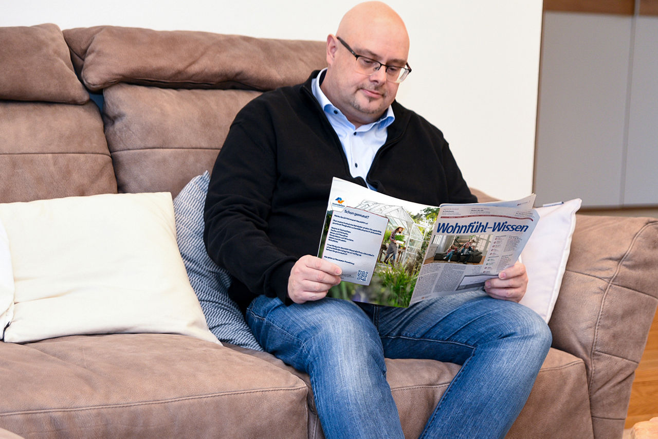 Mann mit Brille sitzt mit einer Zeitung auf einem Sessel und liest