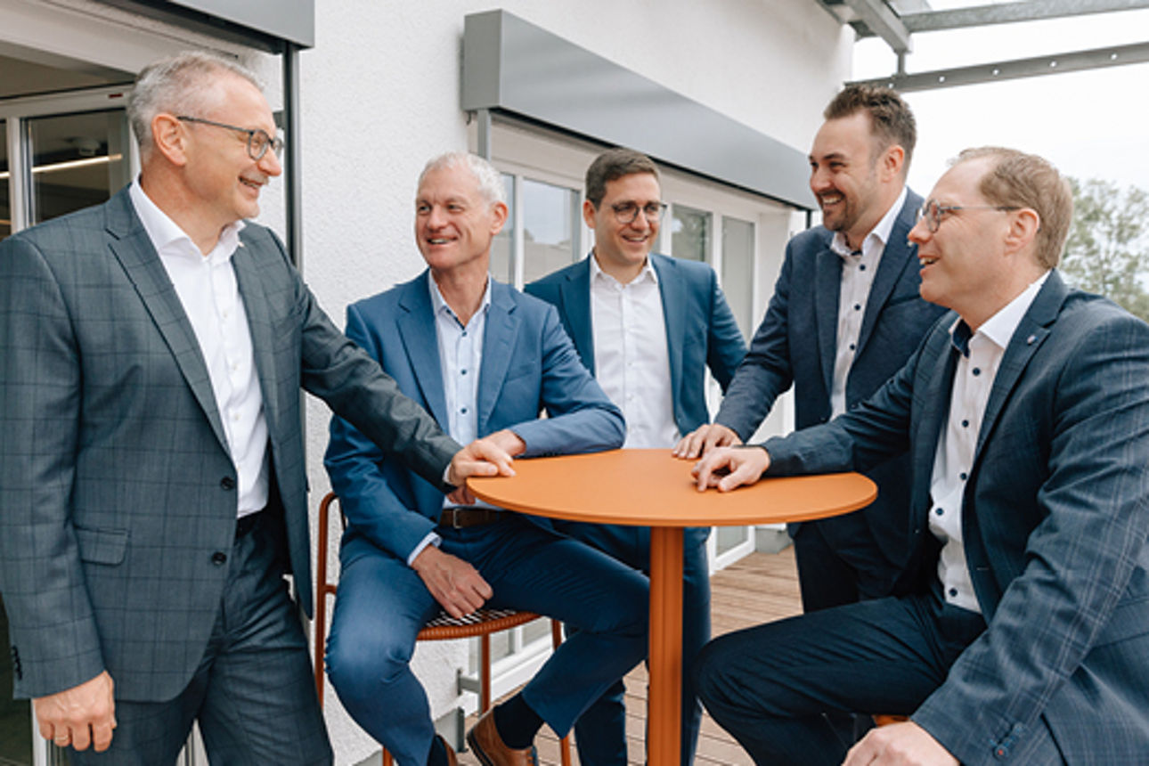 Unsere fünf Männer im Führungskreis sind im lockeren Gespräch an einem orangen Stehtisch.
