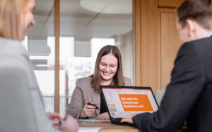 Eine Gruppe von drei Personen sitzt an einem Tisch in einem modernen Büro und arbeitet zusammen.