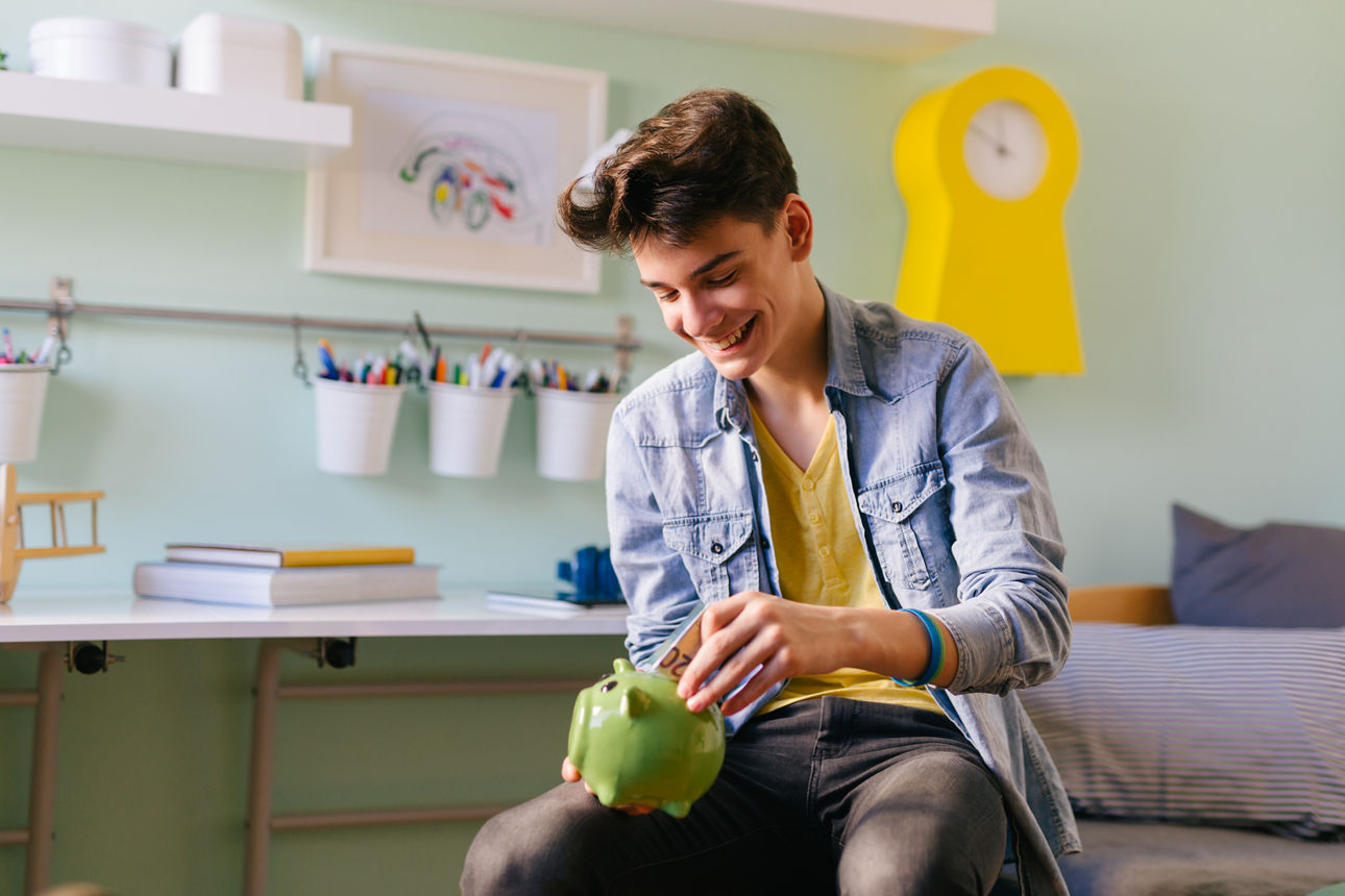 Ein Kind sitzt mit seiner Spardose auf seinem Bett im Kinderzimmer